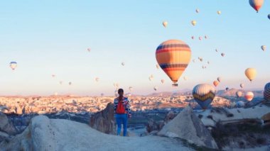 Sırt çantalı yolcu hava balonlarına bakıyor. Sportif kız ve bir sürü sıcak hava balonu. Tam özgürlük, başarı, başarı, mutluluk hissi.