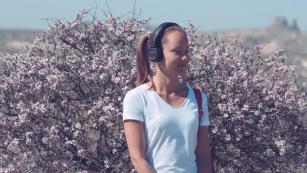 Жіноча модель з навушниками в парку. Молода, красива дівчина з довгим волоссям на фіолетовому фоні . — стокове відео