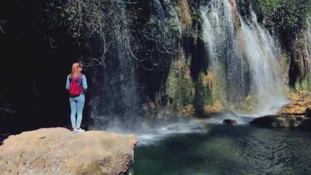 Antenne. Vrijheid jonge reiziger vrouw met rode rugzak reis naar verbazingwekkende prachtige waterval in tropisch regenwoud — Stockvideo