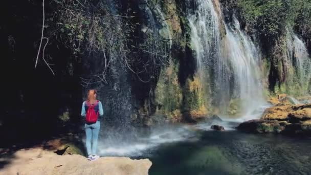 AERIAL. Liberdade Jovem viajante mulher com mochila vermelha viajar para incrível bela cachoeira na floresta tropical — Vídeo de Stock