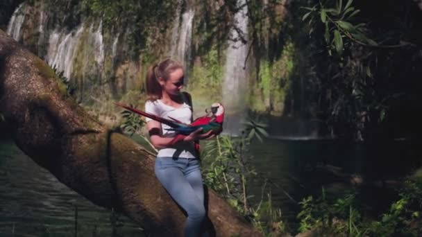 Woman playing with parrots in jungle with faterfall on background — Stock Video