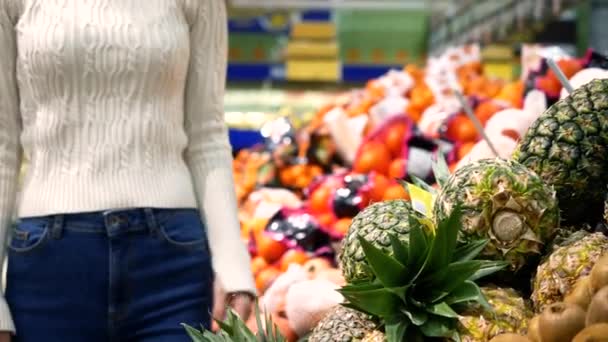 The beautiful asian woman choosing fresh pineapples in shop. Holds with a hand pineapple — Stock Video