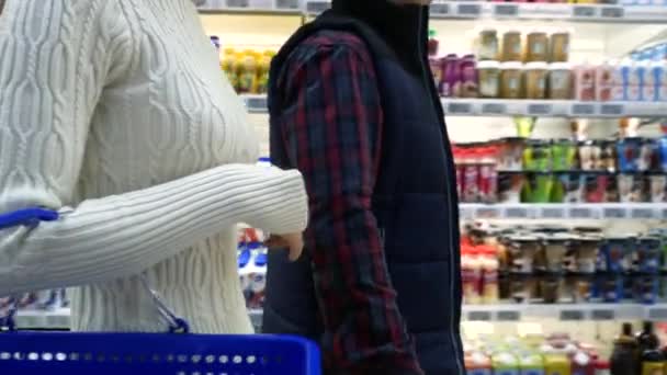 Casal em um supermercado de compras equipado com um carrinho de compras comprando mantimentos e outras coisas, eles estão procurando o que precisam — Vídeo de Stock