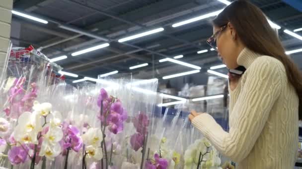 Mujer asiática joven eligiendo flor de orquídea en el supermercado. Compras, consumismo y concepto de personas . — Vídeos de Stock