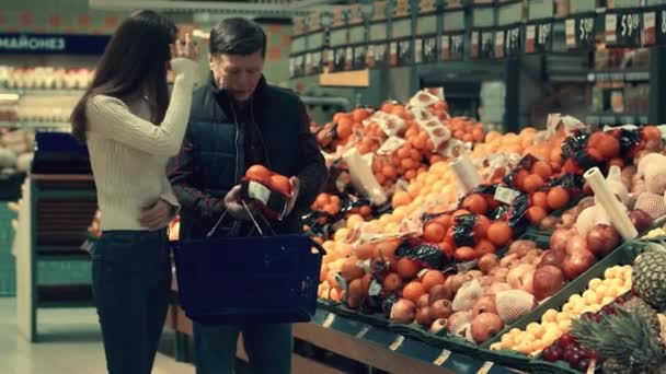 Familie wählt Produkte im Supermarkt und lacht. Mann erklärt, welcher Orangenkönig besser ist. — Stockvideo