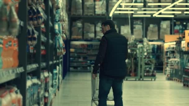 In de supermarkt: man duwen winkelwagentje door verse producten sectie van de winkel. Volgende back View shot. — Stockvideo
