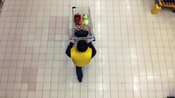 Un magasinier pousse un chariot le long d'une allée de supermarché - Vue du haut . — Video