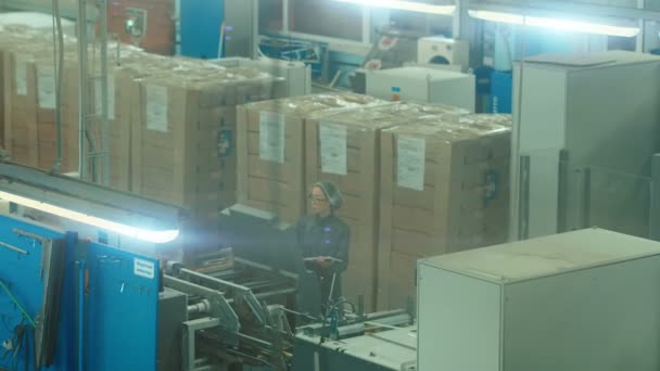 На фабрике высоких технологий азиатская женщина-инженер использует учебник по программированию для выбора и размещения станков. Внутри огромного производственного склада . — стоковое видео