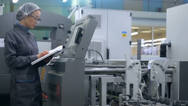На заводе высоких технологий азиатская женщина-инженер использует компьютер для выбора программ и размещения электронных машин . — стоковое видео