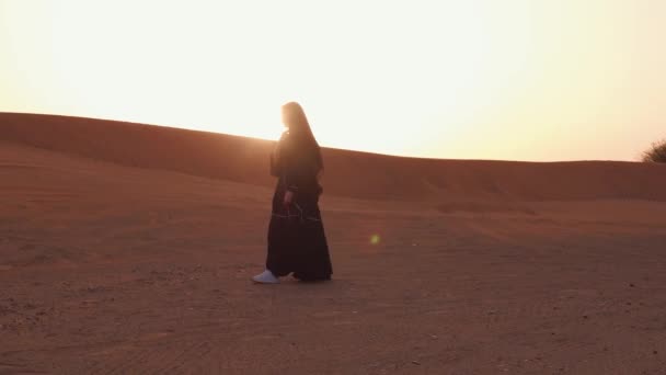 Retrato de una joven árabe vestida con ropa negra tradicional durante el hermoso atardecer sobre el desierto. — Vídeos de Stock