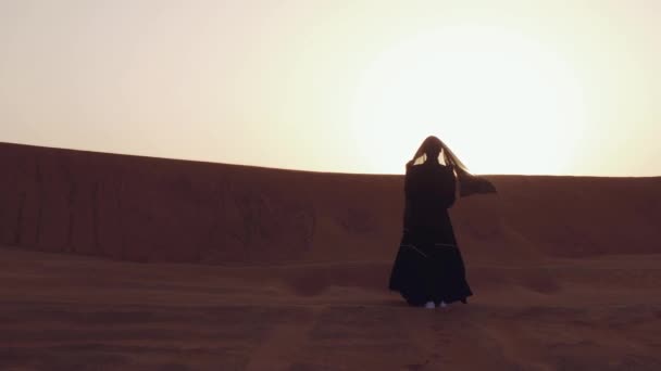 Retrato de una joven árabe vestida con ropa negra tradicional durante el hermoso atardecer sobre el desierto. — Vídeos de Stock