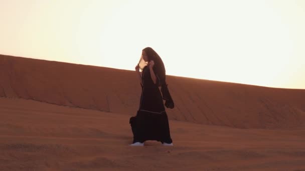 砂漠の上の美しい夕日の間に伝統的な黒い服を着た若いアラブ人女性の肖像画. — ストック動画