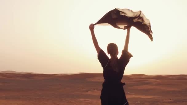 Una donna con una sciarpa nera tra le mani in dune di sabbia in un deserto — Video Stock