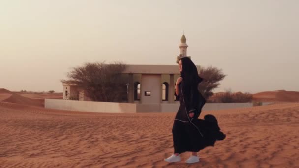 Retrato de una joven árabe vestida con ropa negra tradicional durante el hermoso atardecer sobre el desierto. — Vídeo de stock