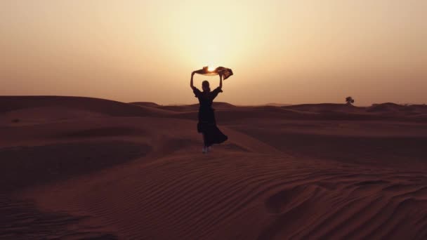 Μια γυναίκα με ένα μαύρο κασκόλ στα χέρια της σε αμμόλοφους σε μια έρημο — Αρχείο Βίντεο