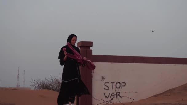 Retrato de una mujer negra con velo frente a un desierto blanco y edificio. Detener la inscripción de guerra y helicópteros en el fondo. — Vídeo de stock