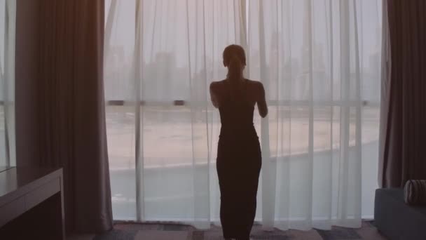 年轻漂亮的女人打开窗帘在慢动作看日出站在窗口，她家附近和享有的市景从高度 — 图库视频影像