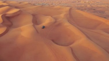 AERİAL. Arabanın üstünde yükseklik uçuşu. Çöl safarisi arabası gün batımında Dubai çölünde kum tepesi.