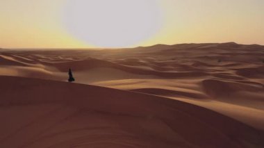 Abaya Birleşik Arap Emirlikleri 'nde bir kadının yanında uçan bir insansız hava aracının hava görüntüsü. Boş Bölge' nin çölünde kumullarda yürüyen geleneksel bir elbise. Abu Dabi, BAE.