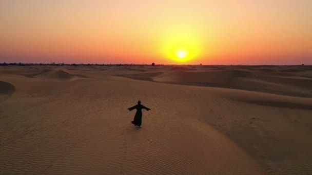 Luchtfoto van een drone vliegen naast een vrouw in Abaya Verenigde Arabische Emiraten traditionele jurk rijzende haar armen op de duinen in de woestijn van het lege kwartier. Abu Dhabi, VAE. — Stockvideo