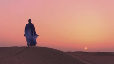 Slowmotion. Çölde gün batımına bakan güzel mavi ve beyaz Arap kıyafetleri giyen kadınlar