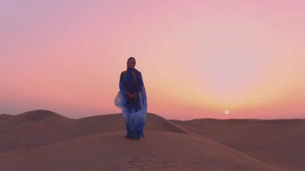 Portrait de belle femme arabe vêtue d'une robe traditionnelle bleue dans le désert au coucher du soleil. — Video