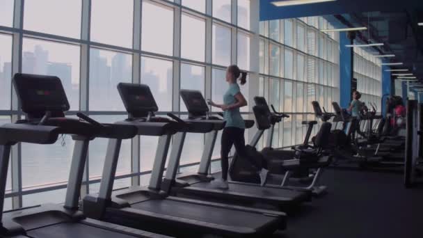 Mujer corriendo en cinta de correr en una ventana panorámica con vista a la ciudad al amanecer. — Vídeos de Stock