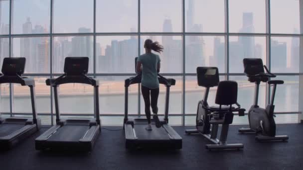 日出时，妇女在全景窗前的跑步机上奔跑，俯瞰全市. — 图库视频影像