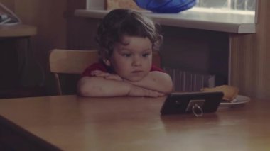 Teknoloji nesli. Mutlu bir çocukluk. Küçük çocuk ağzının suyu akıyor, kahvaltı yapıyor, cep telefonuyla oynuyor. Ev.