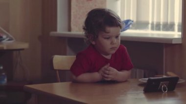 Teknoloji nesli. Mutlu bir çocukluk. Küçük çocuk ağzının suyu akıyor, kahvaltı yapıyor, cep telefonuyla oynuyor. Ev.
