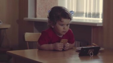 Teknoloji nesli. Mutlu bir çocukluk. Küçük çocuk ağzının suyu akıyor, kahvaltı yapıyor, cep telefonuyla oynuyor. Ev.