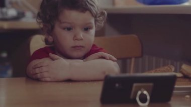 Teknoloji nesli. Mutlu bir çocukluk. Küçük çocuk ağzının suyu akıyor, kahvaltı yapıyor, cep telefonuyla oynuyor. Ev.