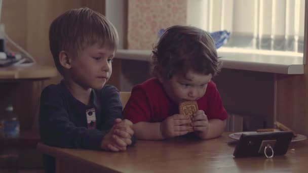 Enciende este. Adorable foto de dos niños mayores diferentes sentados uno al lado del otro y centrando su atención en una pantalla de un teléfono inteligente mientras ambos escuchan música en casa . — Vídeos de Stock