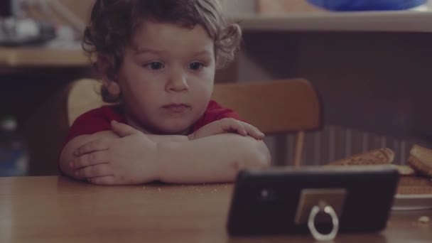 Generación tecnológica. Feliz infancia. Niño pequeño boca sucia babeando, desayunando jugando con el teléfono móvil en la mesa. Hogar. . — Vídeos de Stock