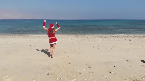 AERIAL. Mulher feliz bonita na Sra. Claus custume na praia tropical, Natal e ano novo férias conceito . — Vídeo de Stock