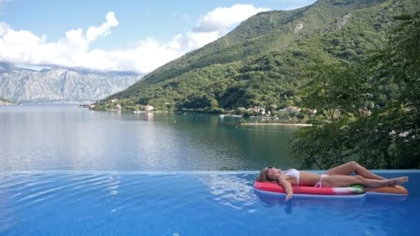 Gyönyörű fiatal karcsú szőke lány pihen egy üdülőhelyen úszás a medencében — Stock videók