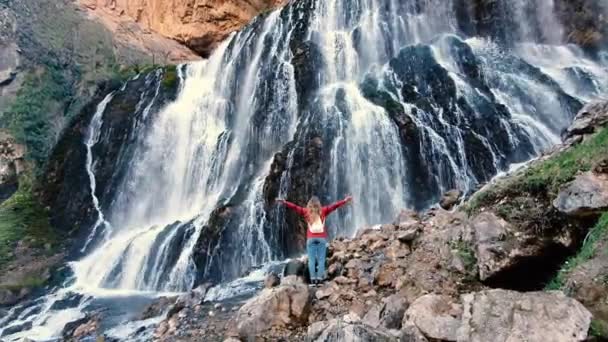 巨大な滝を見ている女性。滝の近くで手を上げて — ストック動画
