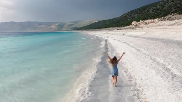 AERİAL. Kız beyaz kumlu plajda koşar ve ellerini kaldırır.. — Stok video