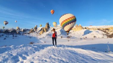 Kışın dağlarda yürüyen bir kadın. Arka planda sıcak hava balonları.
