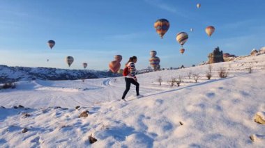 Kışın dağlarda yürüyen bir kadın. Arka planda sıcak hava balonları.