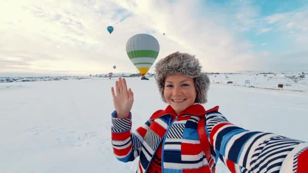 Das Mädchen winkt mit der Hand und grüßt per Videoübertragung. Heißluftballons im Hintergrund. — Stockvideo