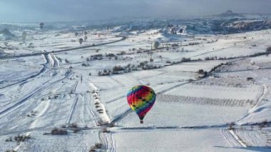 AERİAL. Kış manzarasının üzerinde uçan renkli sıcak hava balonunun üst görüntüsü. 