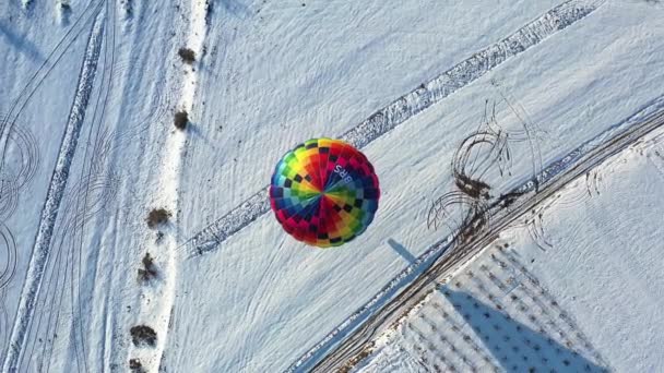 AERIAL. Horní pohled na barevný horkovzdušný balón letící nad zimní krajinou. — Stock video