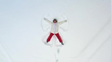 Karda yatan genç bir kız bir melek çiziyor. Kamera etrafında dönüyor ve ona zum yapıyor. Noel Tatilleri.