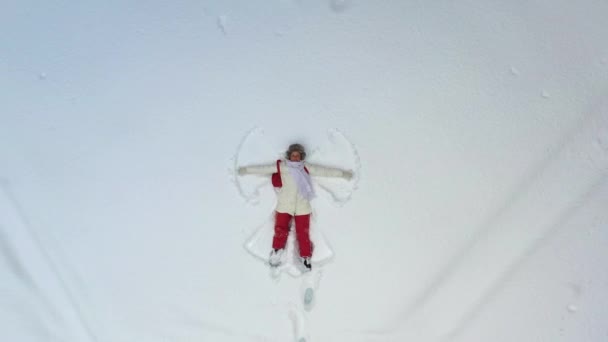 Ein junges Mädchen, das im Schnee liegt, malt einen Engel. Die Kamera schwenkt herum und zoomt auf sie. Weihnachtsferien. — Stockvideo