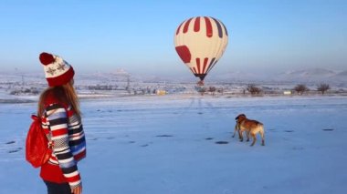 Kışlık kıyafetler giymiş genç bir kadın sıcak hava balonlarına ve neşeli köpeklere bakıyor. İnanılmaz seyahat konsepti. 