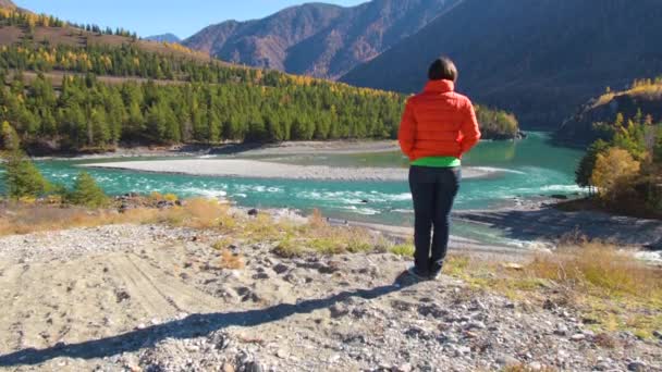 Жінка стоїть біля річки з видом на гори — стокове відео