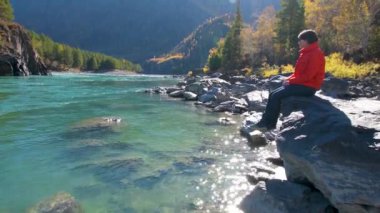 Dağ manzaralı bir nehrin yanında bir kadın oturur
