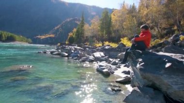 Dağ manzaralı bir nehrin yanında bir kadın oturur