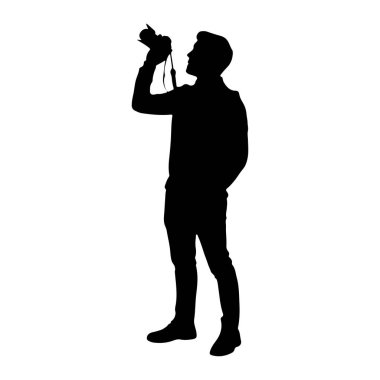 Beyaz bir arkaplana karşı duran siyah bir siluet. Gözüne bir kamera dayamış, fotoğraf çekiyormuş gibi görünüyor. Adam rahat kıyafetler giyiyor. Pantolon ve ayakkabılar da dahil. Bir eli cebinde..